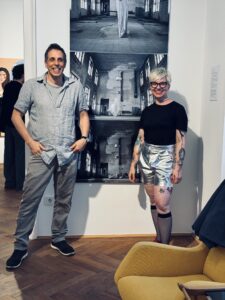 Zwei Personen stehen je links und rechts vor einem großen Foto-Tryptichon in einer Ausstellung